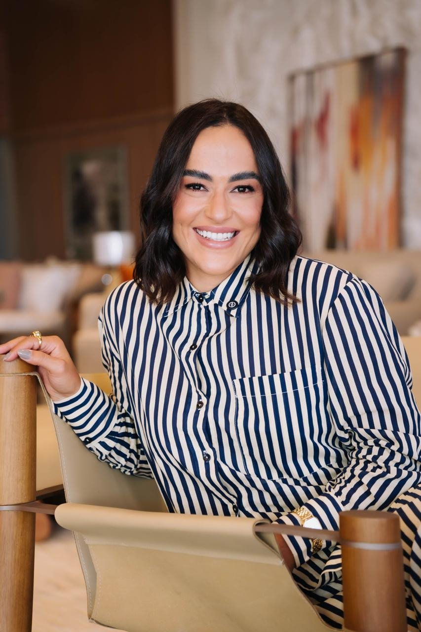 Camila Meneses sentada em uma poltrona, sorrindo